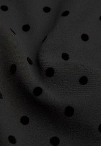 Sort stof med jævnt fordelt fløjlstrukturerede sorte polka dots og synlige bløde folder, som skaber en tekstureret overflade.