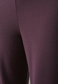 Lila leggings i ett slätt, texturerat tyg, med en närbild av sömmarna och konturerna, som visar materialets töjbarhet.