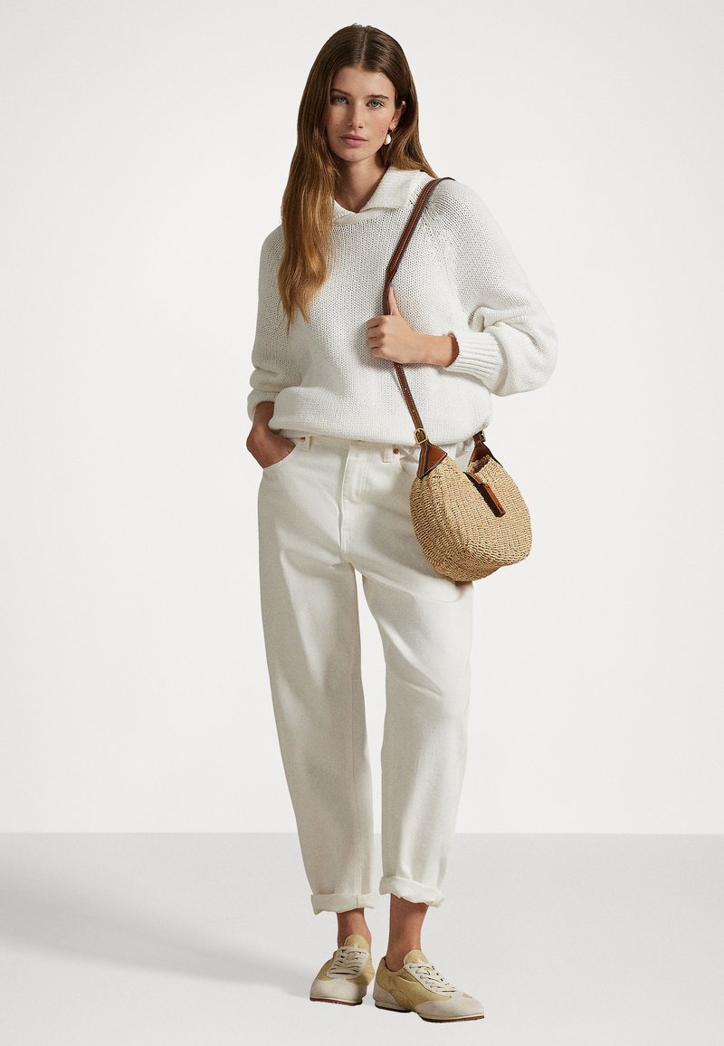 Weißer Strickpullover mit Kapuze, lässige weiße Hose, beige Sneakers und eine kleine geflochtene Umhängetasche mit braunen Akzenten.