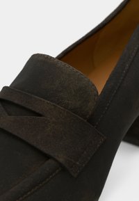 Σκούρα καστανά δερμάτινα loafers με υφή στο επάνω μέρος, επίπεδη σιλουέτα και διακριτικό λουράκι με στρώσεις μπροστά.