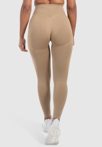 Väldigt höga, beige leggings gjorda av stretchigt tyg, med ribbad yta och åtsittande design. Kombinerat med vita träningsskor.