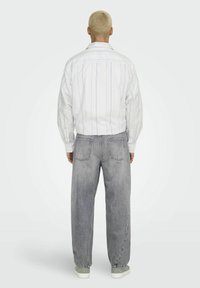 Wit gestreepte longsleeve shirt, grijze losse jeans met twee achterzakken, en lichtgrijze sneakers. De textuur lijkt soepel en casual.