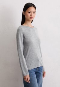 Jasnoszary sweter z długim rękawem, okrągłym dekoltem i gładką teksturą, w połączeniu z niebieskimi dżinsami. Luźny krój, minimalistyczny design bez wzorów.