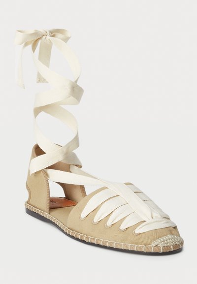 Espadrille de lona beige con cordones de tela blanca, lados abiertos y detalles de textura trenzada a lo largo de la suela. Diseño de punta redonda y plana.