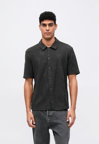 Svart kortermet polo-skjorte med en subtil teksturert mønster, med knappestolpe foran og en avslappet passform. Kombinert med mørke grå jeans.