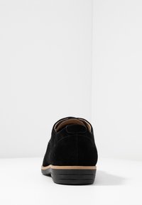 Scarpa in suede nero con un design a profilo basso, caratterizzata da una superficie testurizzata, suola beige in contrasto e un'etichetta sul tallone per una facile vestibilità.