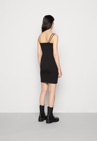 Vestido justo preto com finas alças ajustáveis, silhueta ajustada e comprimento até ao joelho, combinado com botas de tornozelo pretas chunky.