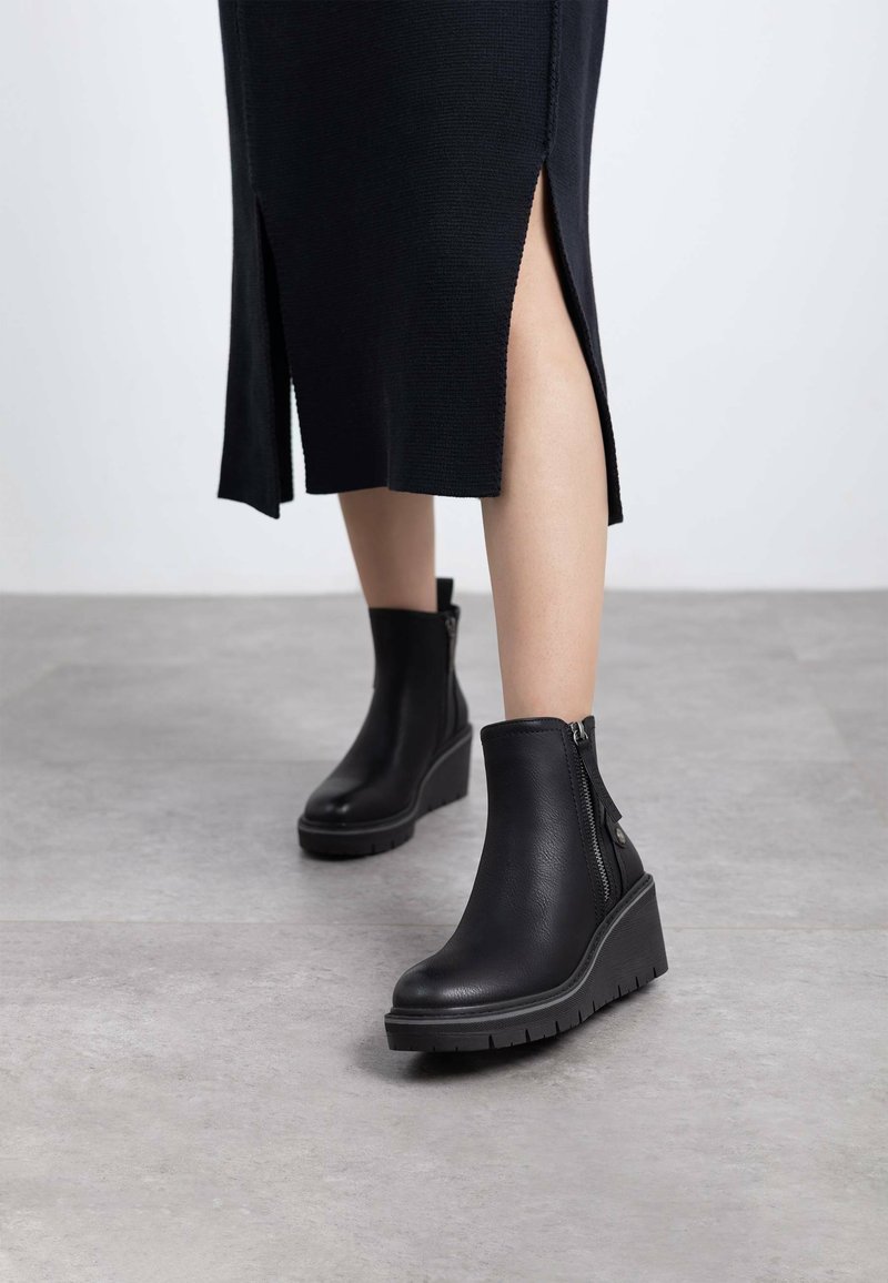 Botines de tacón cuña negros hechos de cuero texturizado, con cremallera lateral, plataforma plana y diseño de punta redonda.