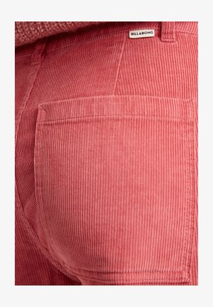 Pink corduroy pants featuring vertical ridges and a back pocket with a label. The fabric has a soft texture and visible stitching details.