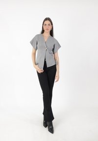 Top gris de manga corta con un escote en V profundo, que presenta un cierre central de botones. Combinado con pantalones negros acampanados y botas negras de punta.