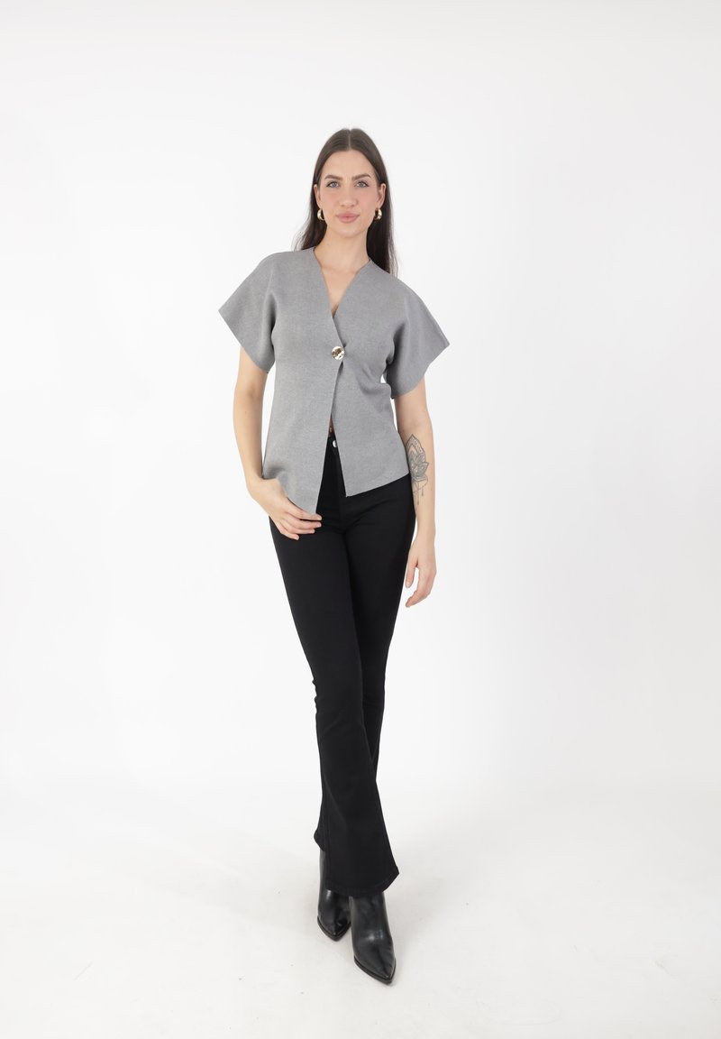 Top gris de manga corta con un escote en V profundo, que presenta un cierre central de botones. Combinado con pantalones negros acampanados y botas negras de punta.