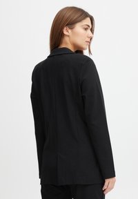 Černý blazer vyrobený z hladké tkaniny. Má klasický límec, uzavírání na jeden knoflík a zadní rozparek pro snadný pohyb.