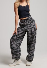 Camo-patroon cargobroek in grijs en zwart, met een relaxte pasvorm, een trekkoord in de taille en grote zijzakken. Gecombineerd met witte sneakers.