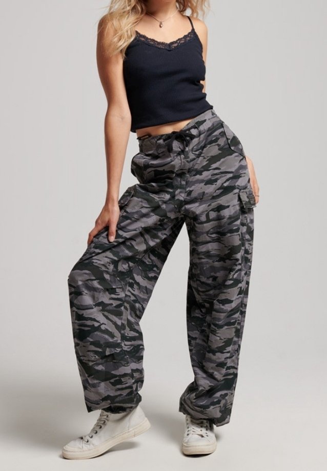 Camo-patroon cargobroek in grijs en zwart, met een relaxte pasvorm, een trekkoord in de taille en grote zijzakken. Gecombineerd met witte sneakers.