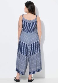 Jumpsuit a righe blu e bianche, con schiena a V e pantaloni larghi. Il tessuto sembra morbido con una leggera texture.