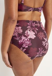 Högt skuren bikiniunderdel i mörk burgunder med rosa blommönster. Materialet är mjukt och elastiskt och har subtila sömdetaljer.