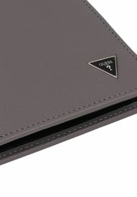 Primo piano di un portafoglio grigio texturizzato con un piccolo logo triangolare Guess nell'angolo.