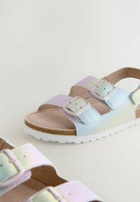 Sandali multicolori con due fibbie regolabili, parte superiore liscia e iridescente, soletta beige morbida e suola in gomma bianca con motivo testurizzato.