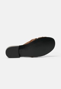 Sandalo in pelle marrone con suola piatta nera. Il design presenta cinturini incrociati e una superficie liscia, adatto per un look informale.