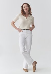 Polo shirt in maglia di colore crema con maniche corte e colletto, abbinato a jeans bianchi a gamba dritta e mocassini marrone chiaro. Design semplice.