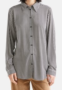 Svartvitt houndstooth-mönstrat knapp-up skjorta med krage och långa ärmar, med avslappnad passform och synliga knappar.