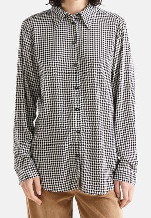 Black and white houndstooth patterned button-up shirt with a collar and long sleeves, featuring a relaxed fit and visible buttons.