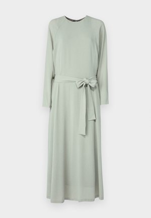 Langærmet kjole i blødt grønt stof med rund halsudskæring, bælte i taljen med sløjfe og en luftig silhuet.