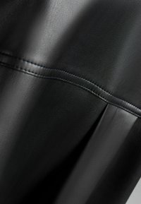 Black leather material with a textured finish, featuring stitched accents and slight folds, highlighting smooth and structured design elements.