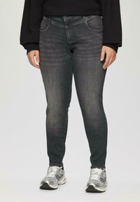 Donkergrijze skinny jeans met een vervaagde textuur, vijf zakken en een knoopsluiting. Draag ze met zilveren sportschoenen.