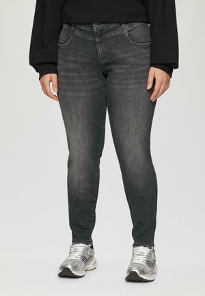 Jean skinny gris foncé avec une texture délavée, cinq poches et une fermeture à bouton. Porté avec des chaussures de sport argentées.