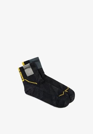 Ein Paar schwarze Knöchelsocken mit grauen und gelben geometrischen Mustern, flach auf einem weißen Hintergrund ausgelegt.