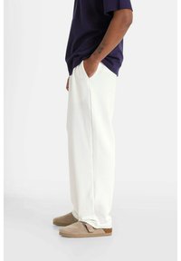 Witte wijde sweatpants met voorzakken, gecombineerd met een donker shirt en lichtbeige instappers. Soepele, zachte textuur overal.
