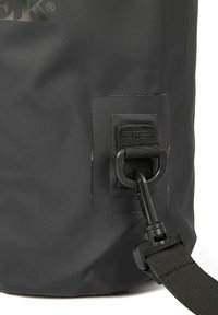 Dettaglio di una borsa impermeabile nera con una tracolla testurizzata, una fibbia in plastica e un attacco a gancio. Il materiale sembra resistente e liscio.
