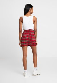 Gonna mini a quadri rossi con un design aderente, realizzata in un tessuto texturizzato e con una piega sul retro, abbinata a una canotta bianca a righe e a sneakers bianche.