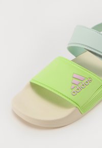 Zelené a svetlomodré šľapky s textúrovaným popruhom, béžovou podrážkou a ružovým logom "adidas". Obsahuje dva nastaviteľné popruhy pre lepšie prispôsobenie.