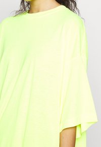 T-shirt oversize giallo neon realizzato in morbido tessuto, con un ampio scollo rotondo e maniche corte e larghe. Colore brillante e vestibilità rilassata.