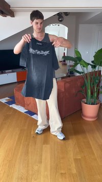 Mustaa ylisuuretta t-paitaa, jossa valkoista koukeroista tekstiä edessä. Lyhyet hihat, pyöreä kaula-aukko. Kevyesti käytetty, esillä vaaleaa taustaa vasten.