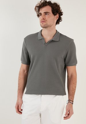 Polo de manga corta gris con un diseño texturizado, cuello acanalado y un ligero detalle en forma de V, combinado con pantalones blancos.
