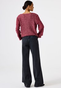 Dieprood gebreid sweater met een textuurpatroon, gecombineerd met brede donkere spijkerbroek. De outfit heeft een ontspannen pasvorm en een hoge halslijn.