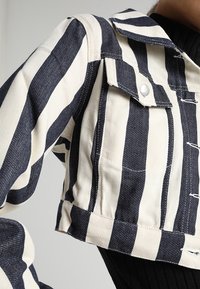 Zkrácená denimová bunda s modro-bílými svislými pruhy, má přední kapsy, špičatý límec a texturovaný materiál.