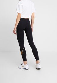 Svarta leggings med en åtsittande design, prydda med en guldlogotyp på det nedre benet, matchade med en vit kortärmad t-shirt och vita träningsskor.