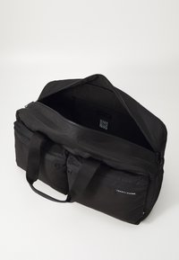 Černá sportovní taška s dvěma předními kapsami, zipy a odolnou tkaninou. Obsahuje webové madla a štítek s QR kódem uvnitř. Jednoduchý design.