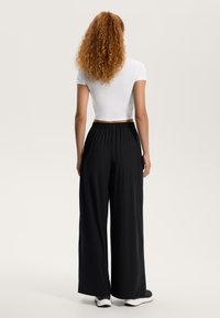 Mustat leveät housut joustavalla vyötäröllä, yhdistettynä tiukkaan valkoiseen lyhythihaiseen paitaan. Kangas näyttää kevyeltä ja sileältä.