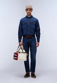 Koszula jeansowa z dwoma kieszeniami na piersi, niebieskie dżinsy i czarne buty. Beżowa dzianinowa czapka, brązowy pasek i kremowa torba z czerwono-czarnym wzorem.