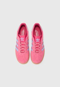 Zapatillas de ante rosa con rayas azul claro, suela de goma y cuello acolchado. Presenta el logo en la lengüeta y el lateral. Estilo atlético clásico.