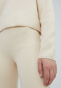 Gebreide set in beige, met een ontspannen fit sweater met ribbels aan de randen en bijpassende, aansluitende broek. Zachte textuur met subtiele variatie.