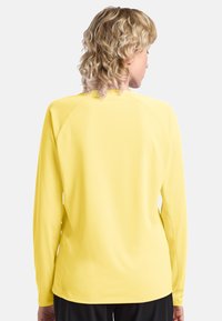 Langarmshirt in leuchtendem Gelb, aus glattem Stoff mit Rundhalsausschnitt und Raglanärmeln. Es hat einen lässigen Schnitt und minimalistische Nähte.