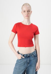 Punane lühike t-särk, mis on valmistatud siledast puuvillast, ümmarguse kaelusega ja lühikeste varrukatega. Kombineeritud helesiniste kõrge vöökohtadega teksadega.