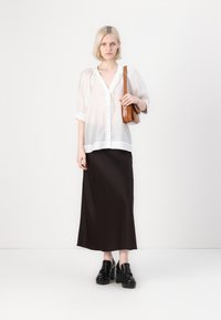 Blusa bianca semi-trasparente con maniche a sbuffo e bordo in pizzo, abbinata a una lunga gonna nera in satin e scarpe platform nere spesse. Borsa marrone.