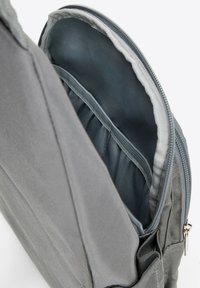 Sac à dos en tissu gris avec fermeture éclair, doté d'une doublure intérieure lisse, de séparateurs de poches et d'une surface extérieure texturée.